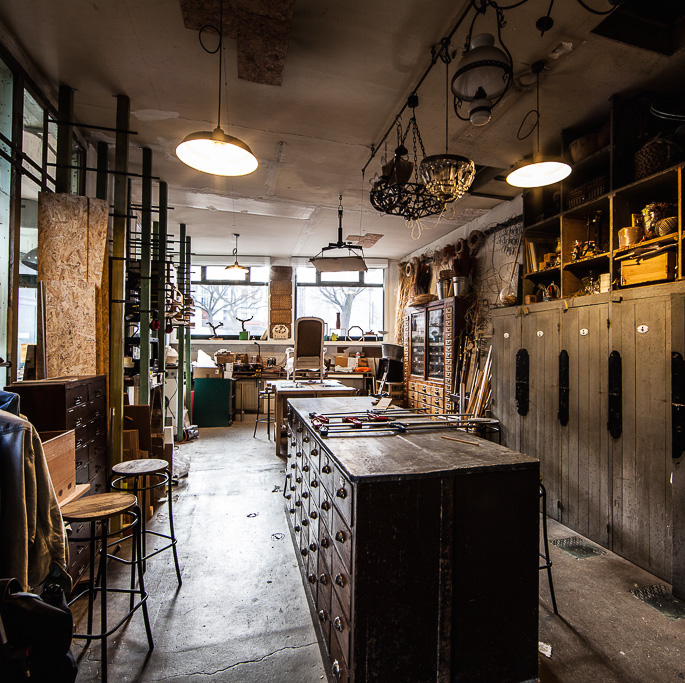 vue de l'atelier du rez-de-chaussée avec une grande table en bois au centre de la pièce et des outils et machines rangés sur des meubles