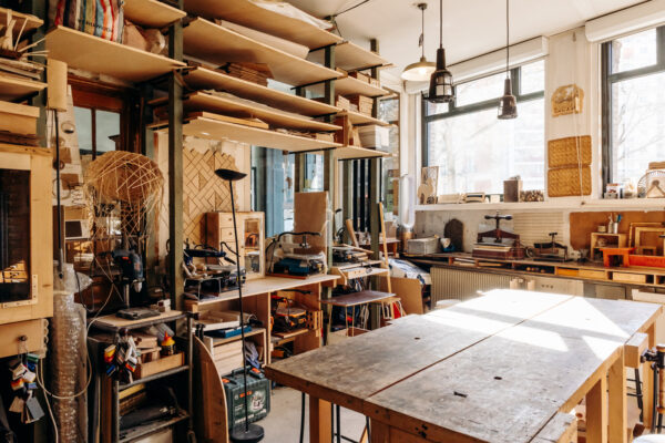 vue de l'atelier du rez-de-chaussée avec une grande table en bois au centre de la pièce et des outils et machines rangés sur des meubles