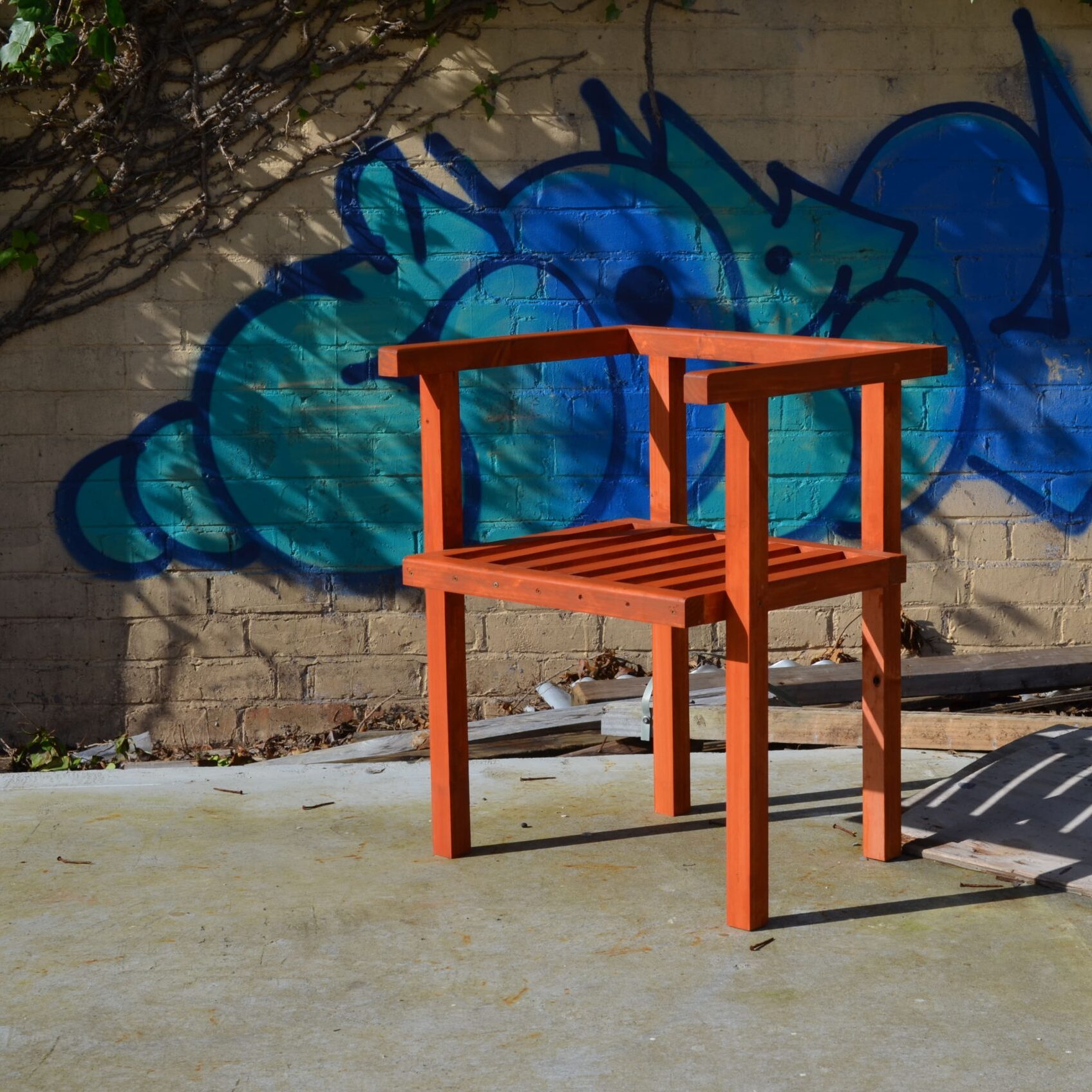 chaise en bois carrée posée au sol dehors avec un graffiti en fond