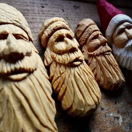 plusieurs visages de pères noël sculptés en bois posés côte à côté
