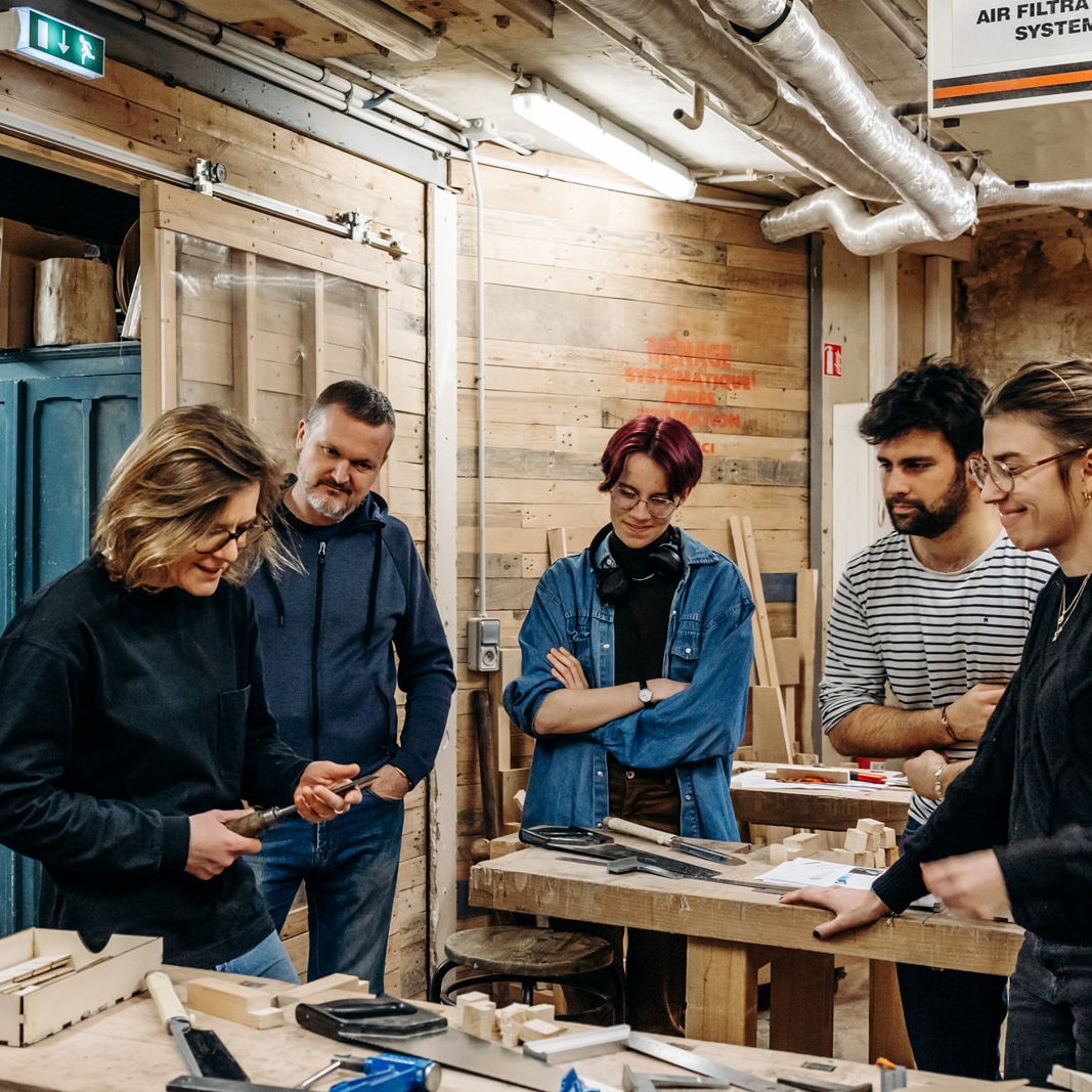 groupe de personnes réunies autour d'un établi dans un atelier en bois avec des outils de menuiserie